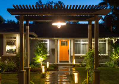 craftsman style pergola framing a lit path to a bold orange front door